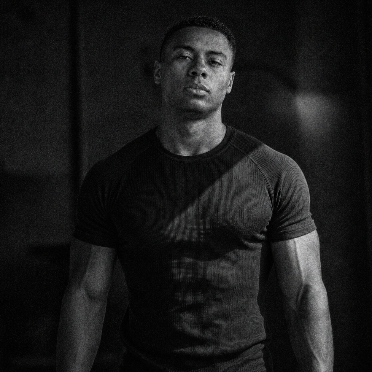 Black and white portrait of a man wearing a fitted t-shirt against a dark background