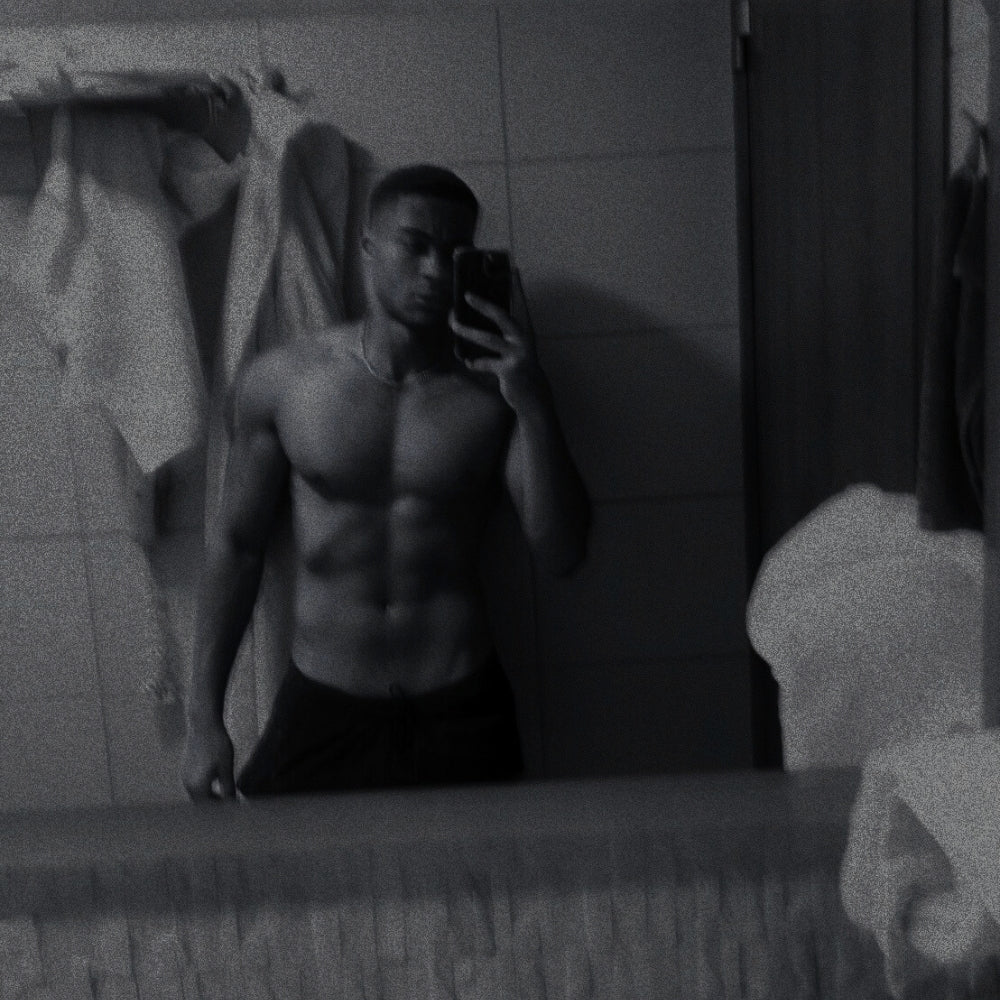 Man taking a mirror selfie in a bathroom, shirtless.